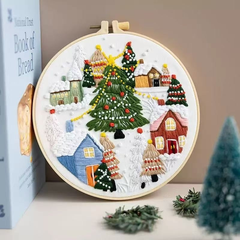 Embroidery hoop with a Christmas-themed design featuring trees and houses on a snowy background.
