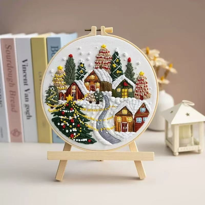 Embroidery hoop with a Christmas village scene on a stand, books in the background