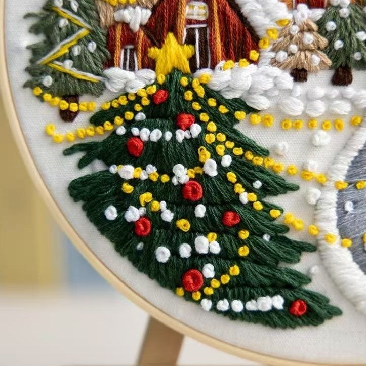 Embroidery hoop with a Christmas-themed design featuring a tree, house, and stars.