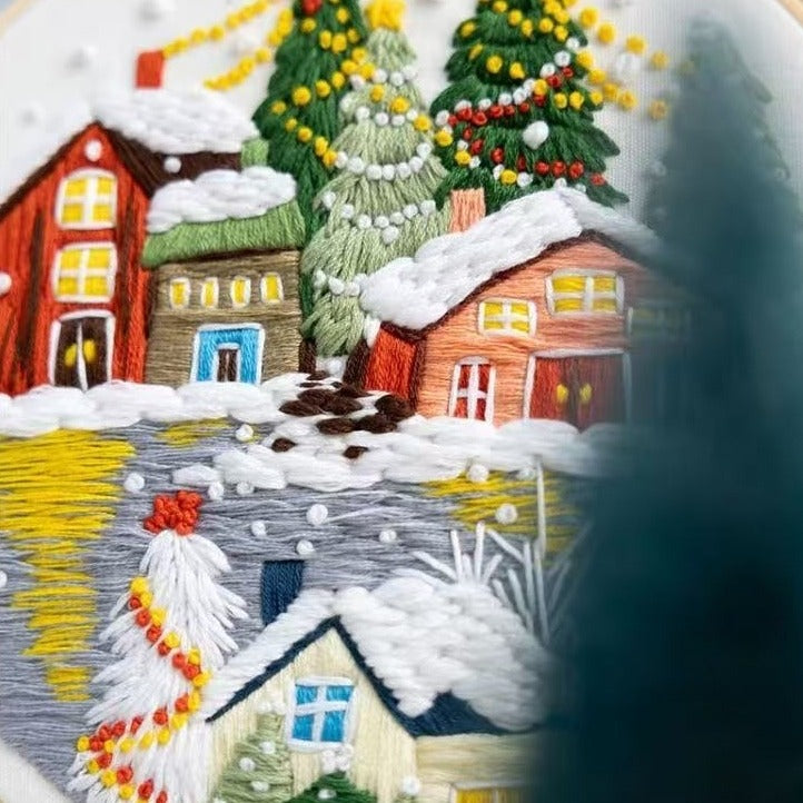 Embroidered scene of a snowy village with houses and trees.