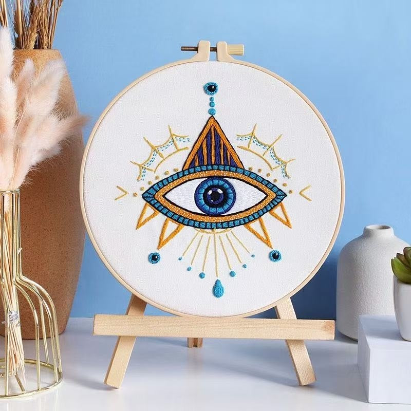 Embroidery hoop with eye design on a stand against a blue background