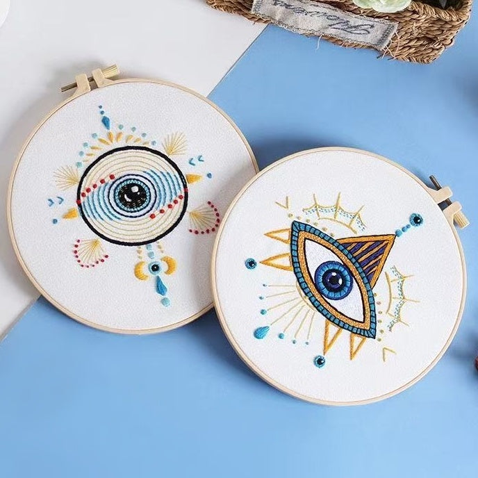 Two embroidery hoops with eye designs on a blue surface