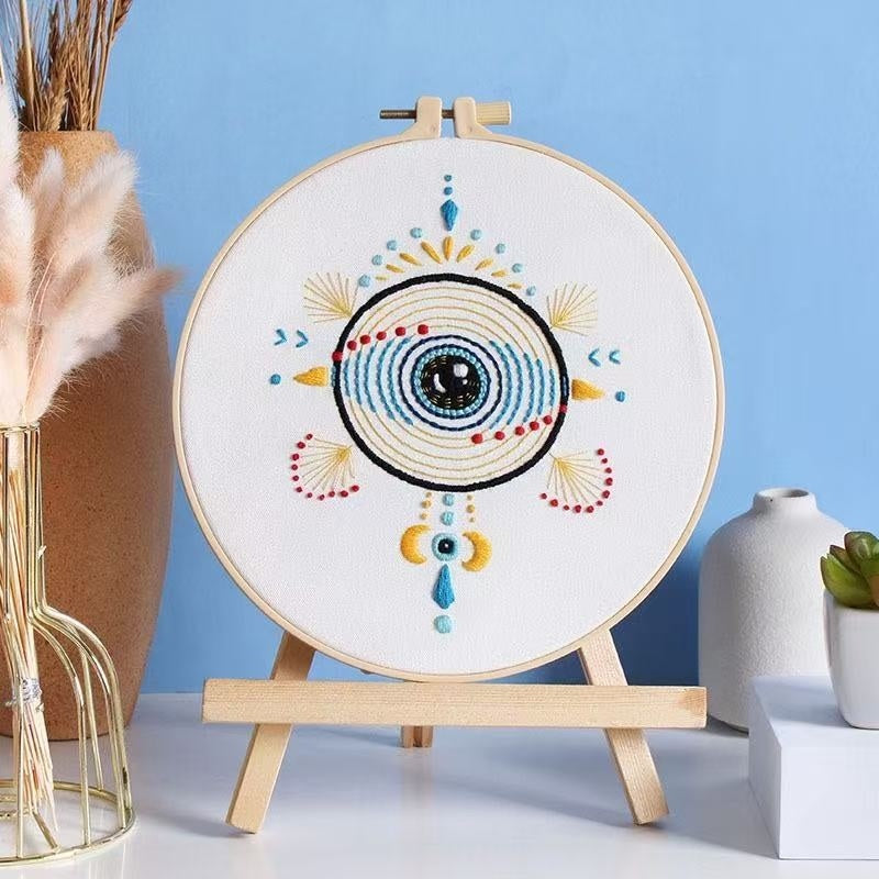 Embroidery hoop with colorful eye design on a stand against a blue background