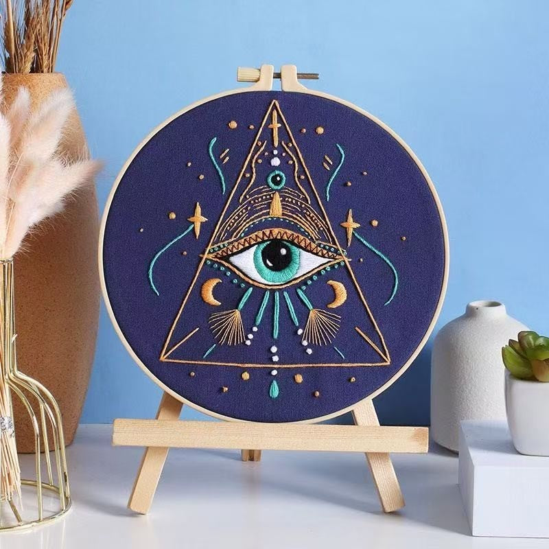 Embroidery hoop with eye design on a stand against a blue background