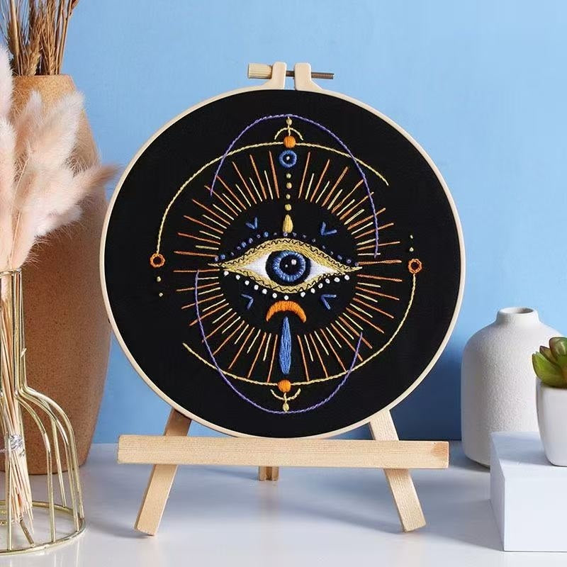Embroidery hoop with eye design on a stand against a blue background