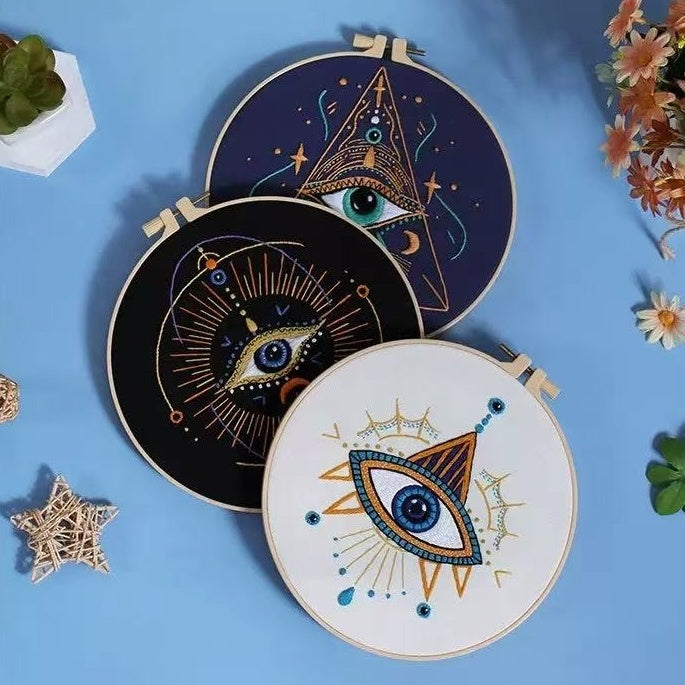 Three embroidery hoops with eye designs on a blue background