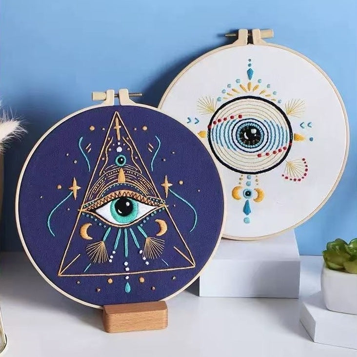 Two embroidery hoops with eye-themed designs on a blue background