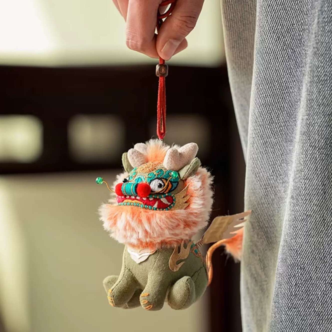 Plush embroidered Chinese beast Kylin toy keychain with red lanyard held by a person