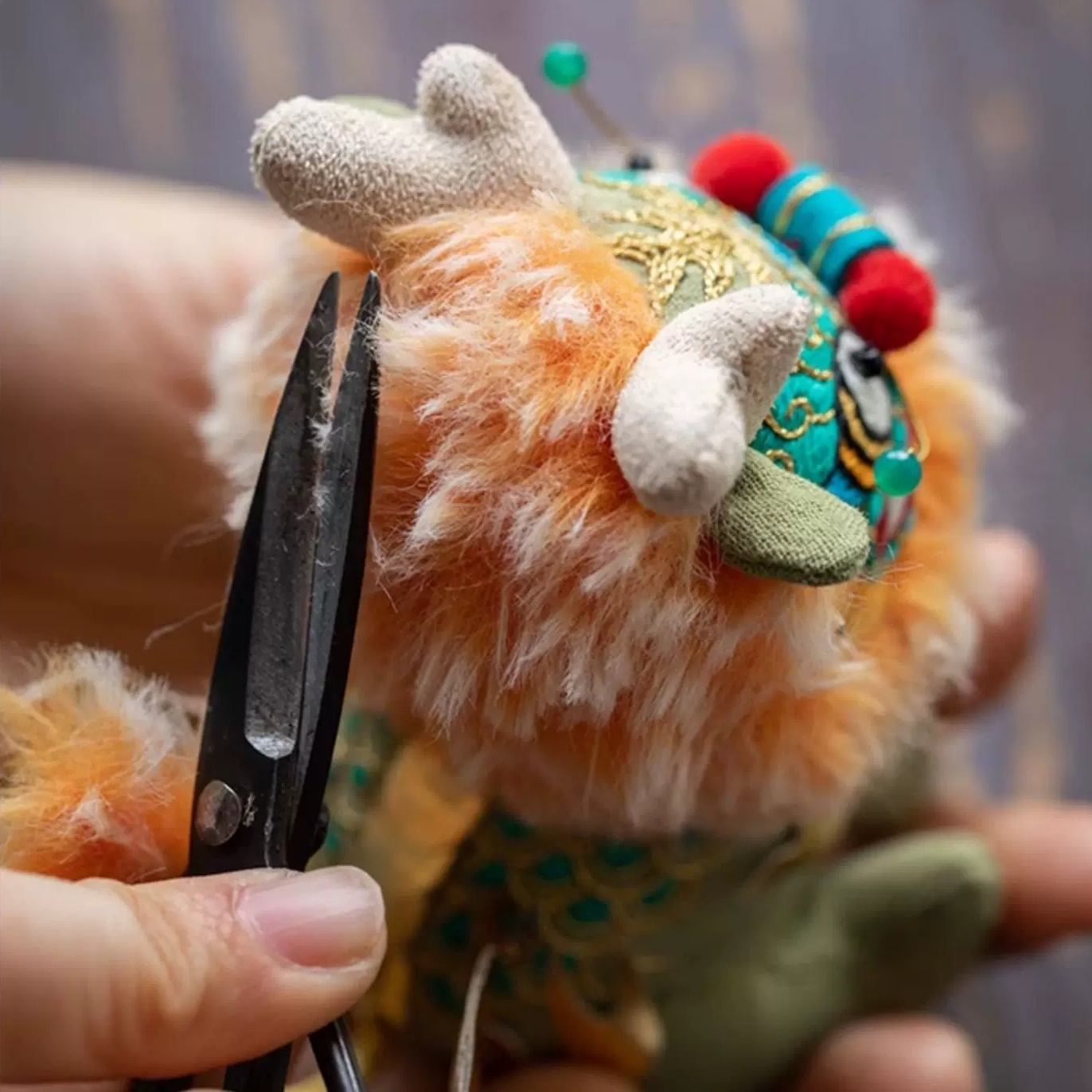 Hand holding a pair of scissors cutting the hair of the embroidered Kylin plush toy doll with colorful details