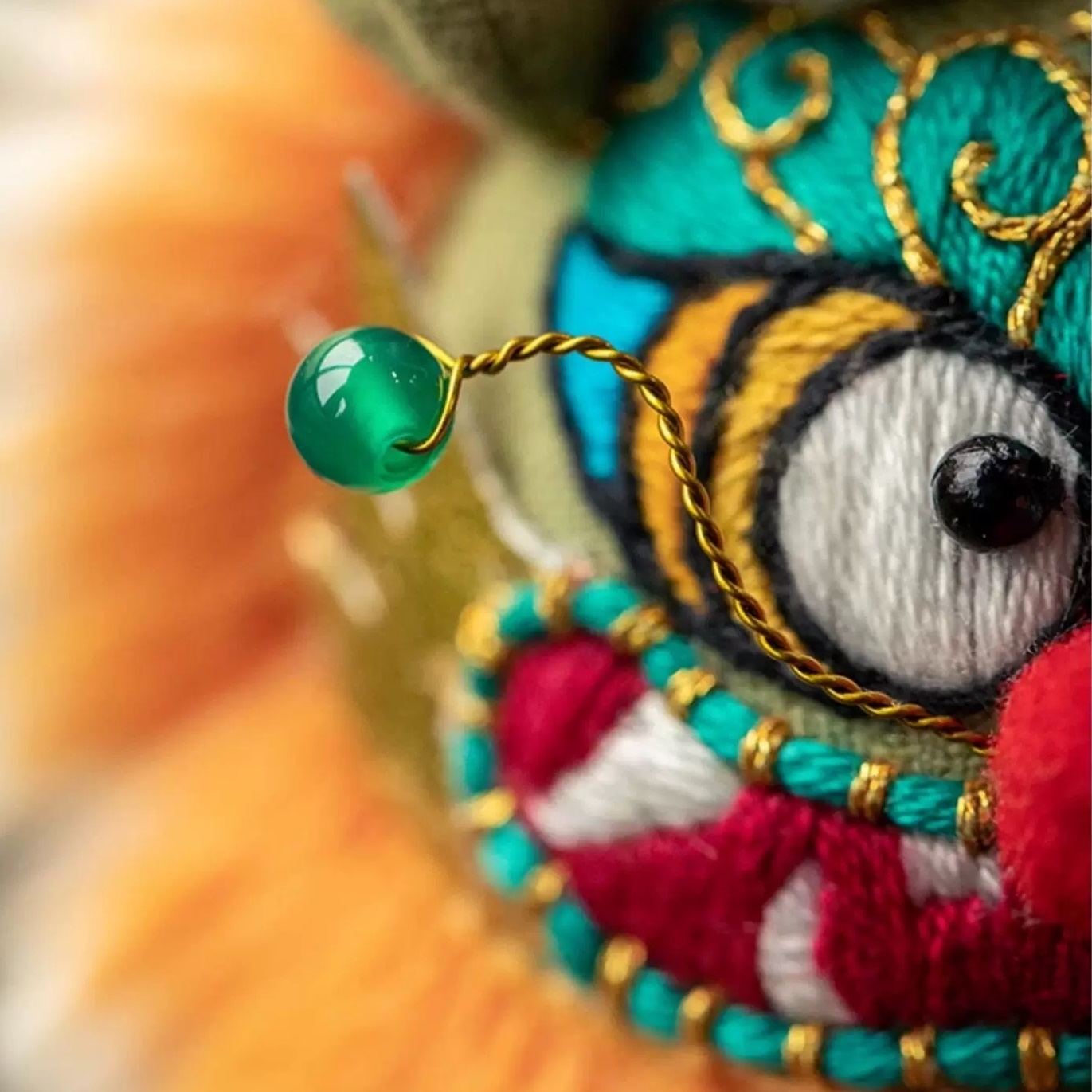 Close-up of a colorful embroidered fabric with intricate patterns and a green bead.