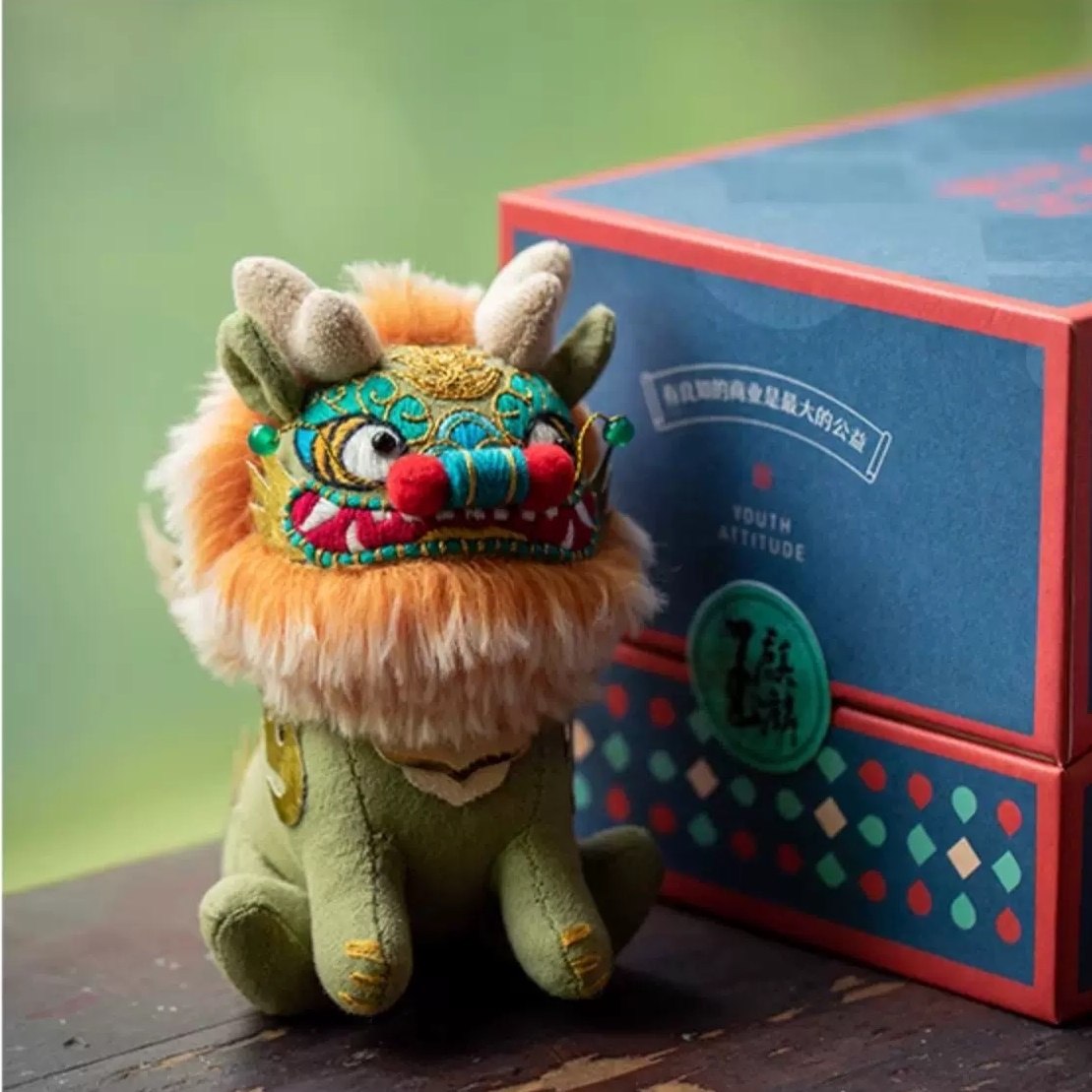 Colorful hand-sewn Chinese beast Kylin plush toy next to a decorative box with a green background