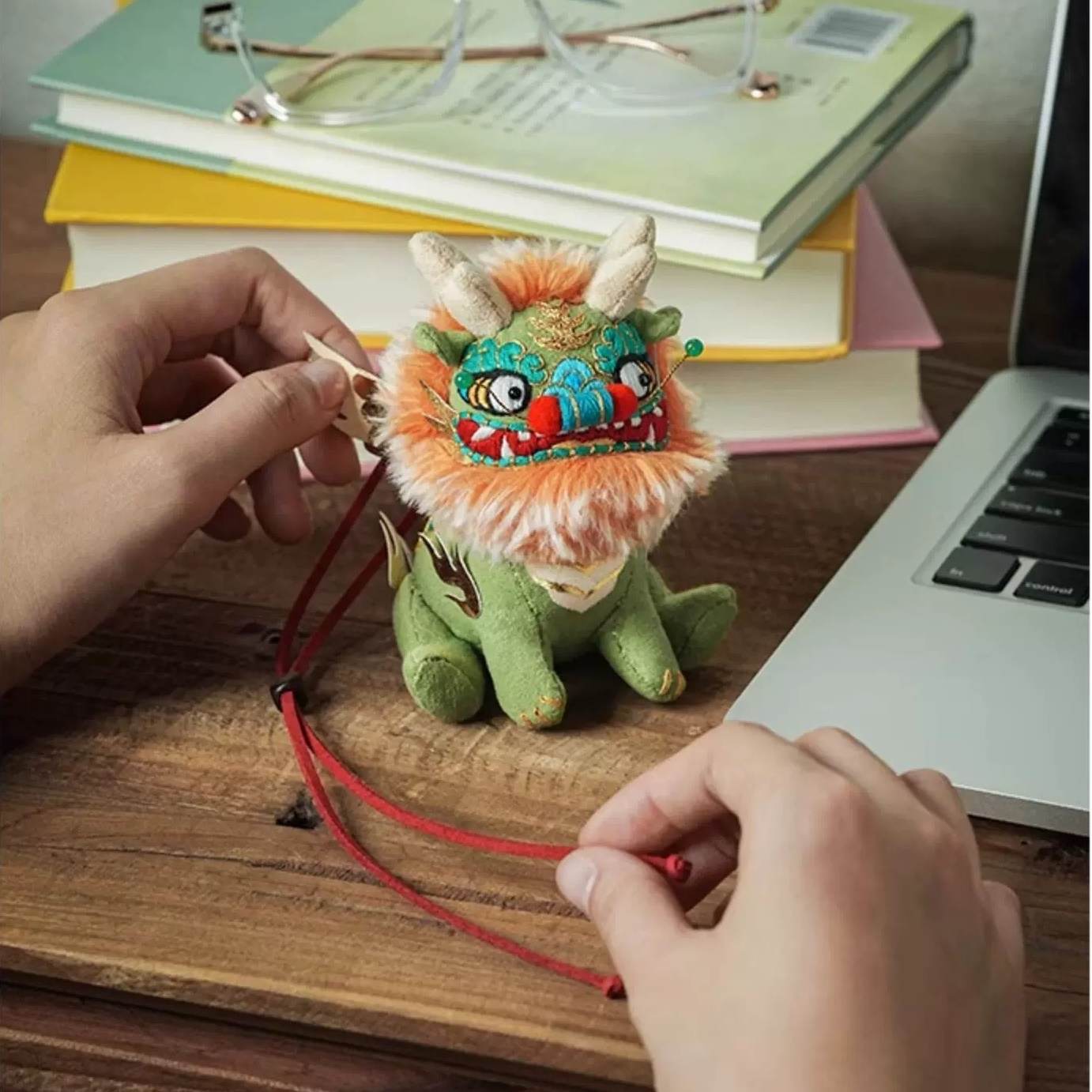Colorful plush Chinese beast Kylin toy doll on a wooden desk with books and a laptop in the background