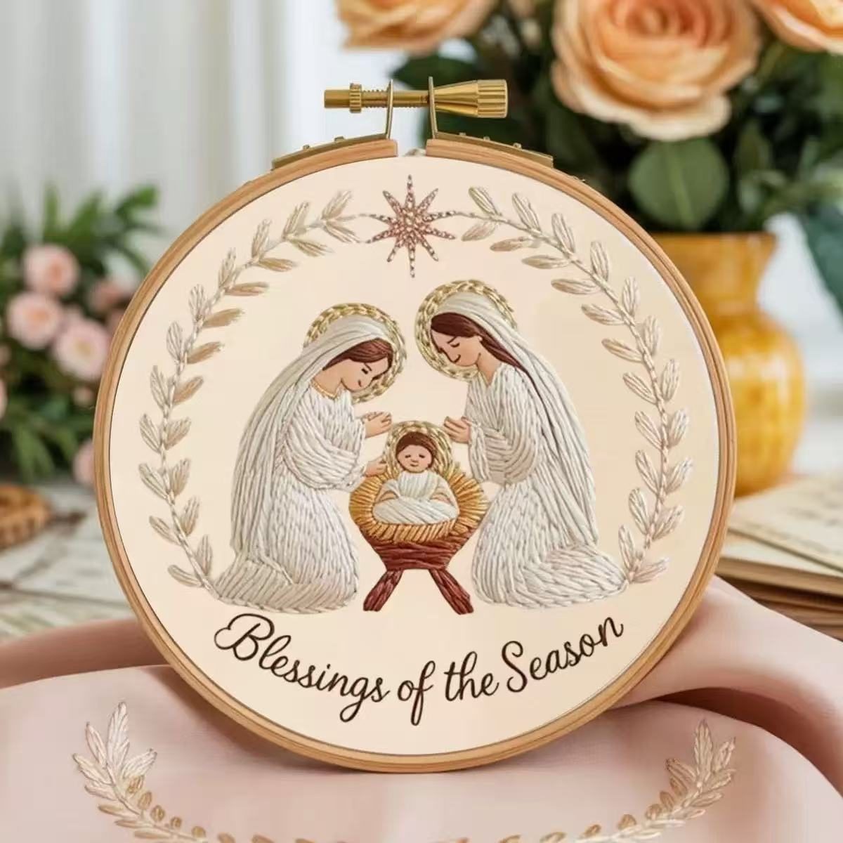 Decorative hoop with nativity scene illustration and 'Blessings of the Season' text, surrounded by flowers.