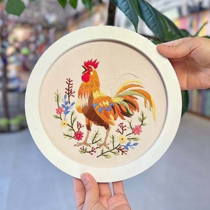 Embroidery hoop with a colorful rooster design held by a hand.