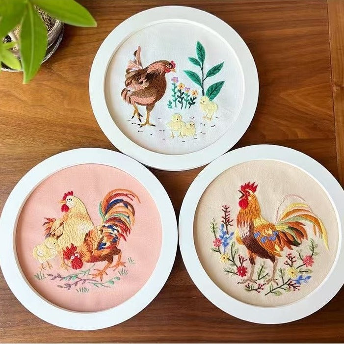 Three embroidered roosters on round white frames on a wooden surface.