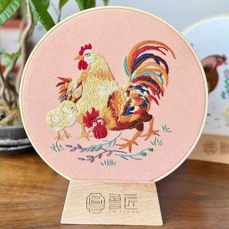 Embroidery of a rooster on a pink background with a wooden stand.
