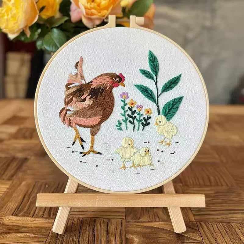 Embroidery hoop with a chicken and chicks design on a wooden stand.
