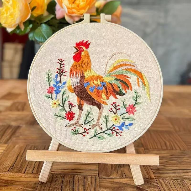 Embroidery hoop with a colorful rooster design on a wooden surface.