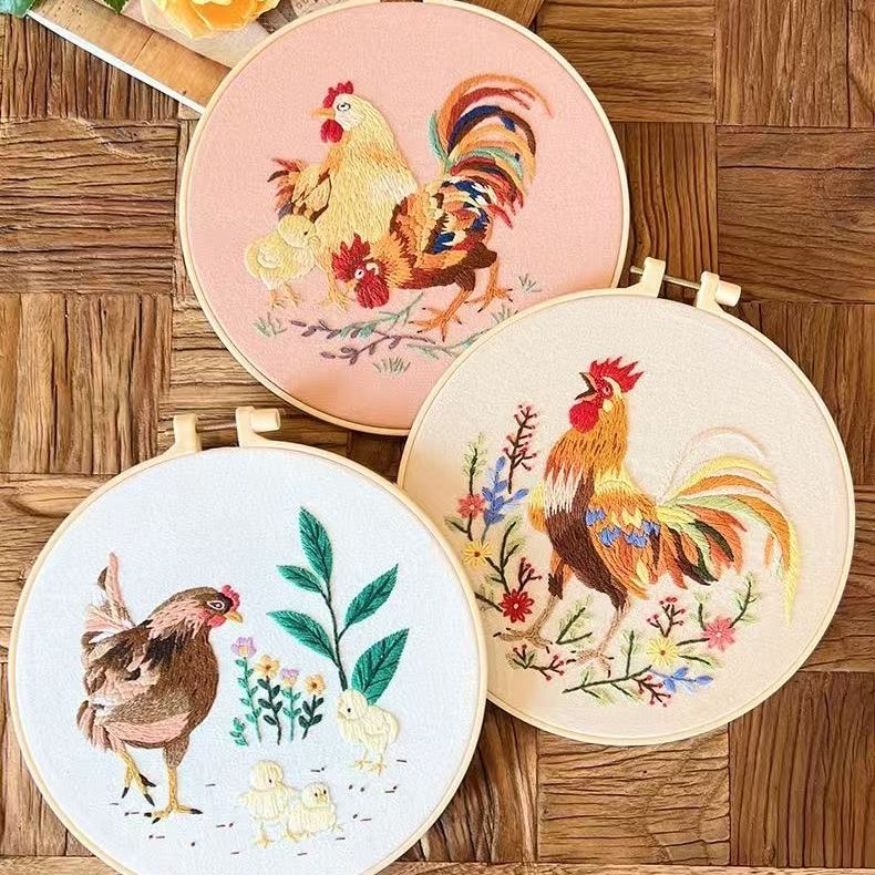 Three embroidered hoops with rooster designs on a wooden surface