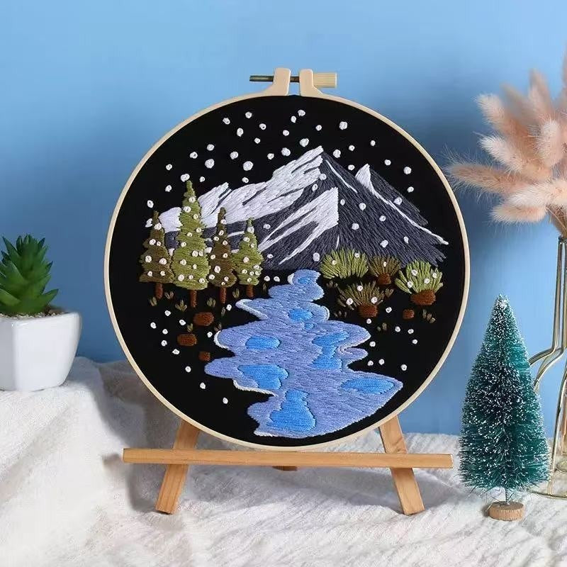 Embroidery hoop with snowy mountain and landscape design on a stand against a blue wall