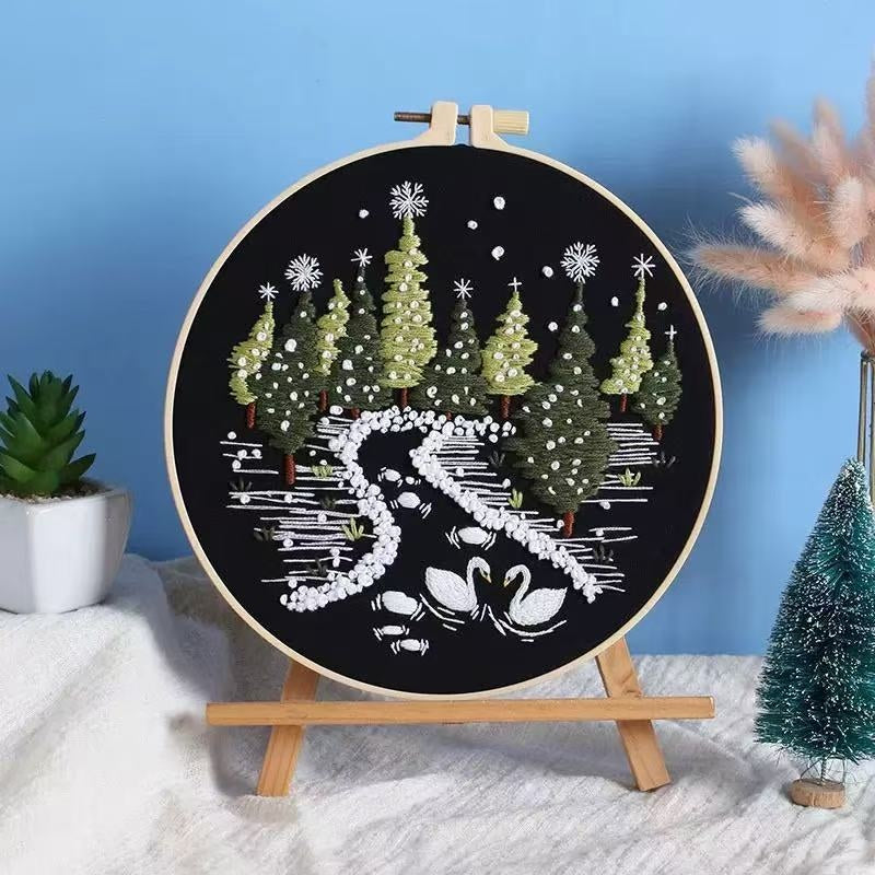 Embroidery hoop with a winter scene design featuring trees and swans on a black background.