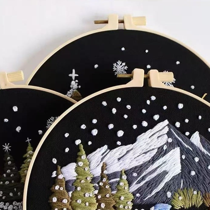 Embroidery hoops with snowy mountain and tree landscape design on a black background