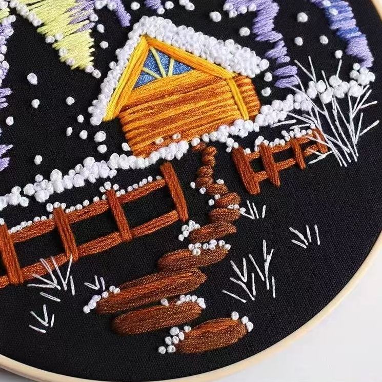 Embroidery of a snowy landscape with a cabin and bridge.