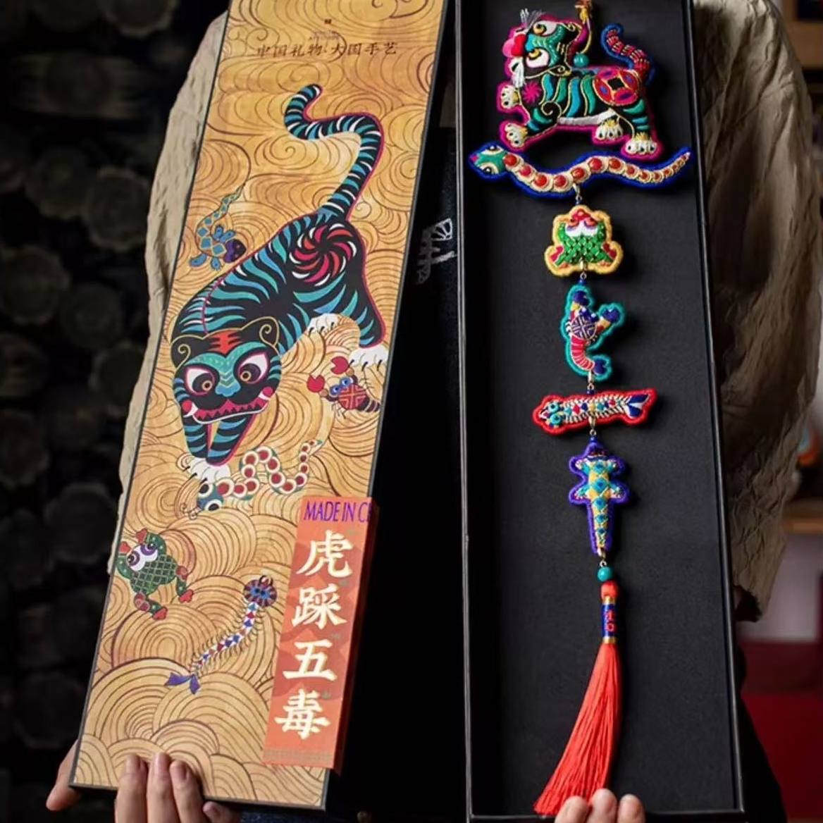 Colorful Chinese decorative tiger and five poisonous creatures amulet with tassel in a gift box held by a person