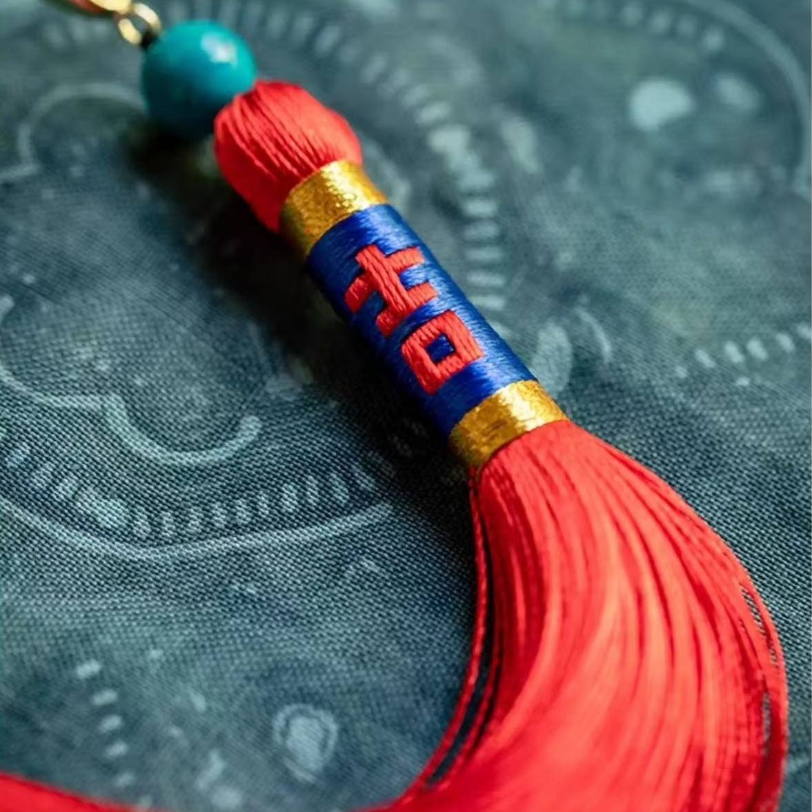 Red tassel with blue and gold accents on a textured fabric background