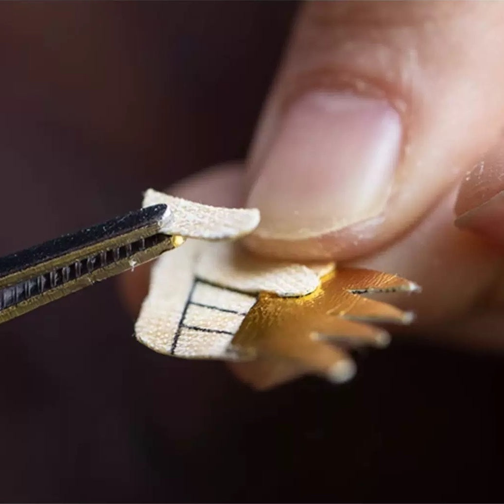 Close-up of a hand holding a small golden component with a black background