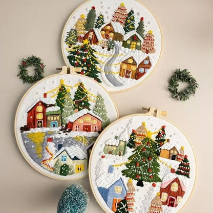 Set of four embroidered Christmas scenes with houses, trees, and wreaths on a beige background.