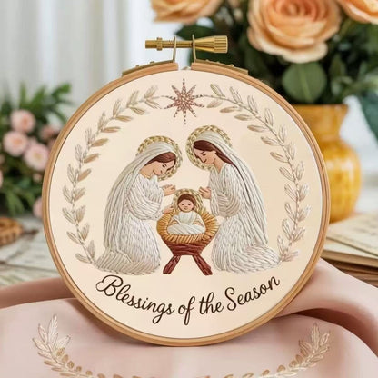 Decorative hoop with nativity scene illustration and 'Blessings of the Season' text, surrounded by flowers.