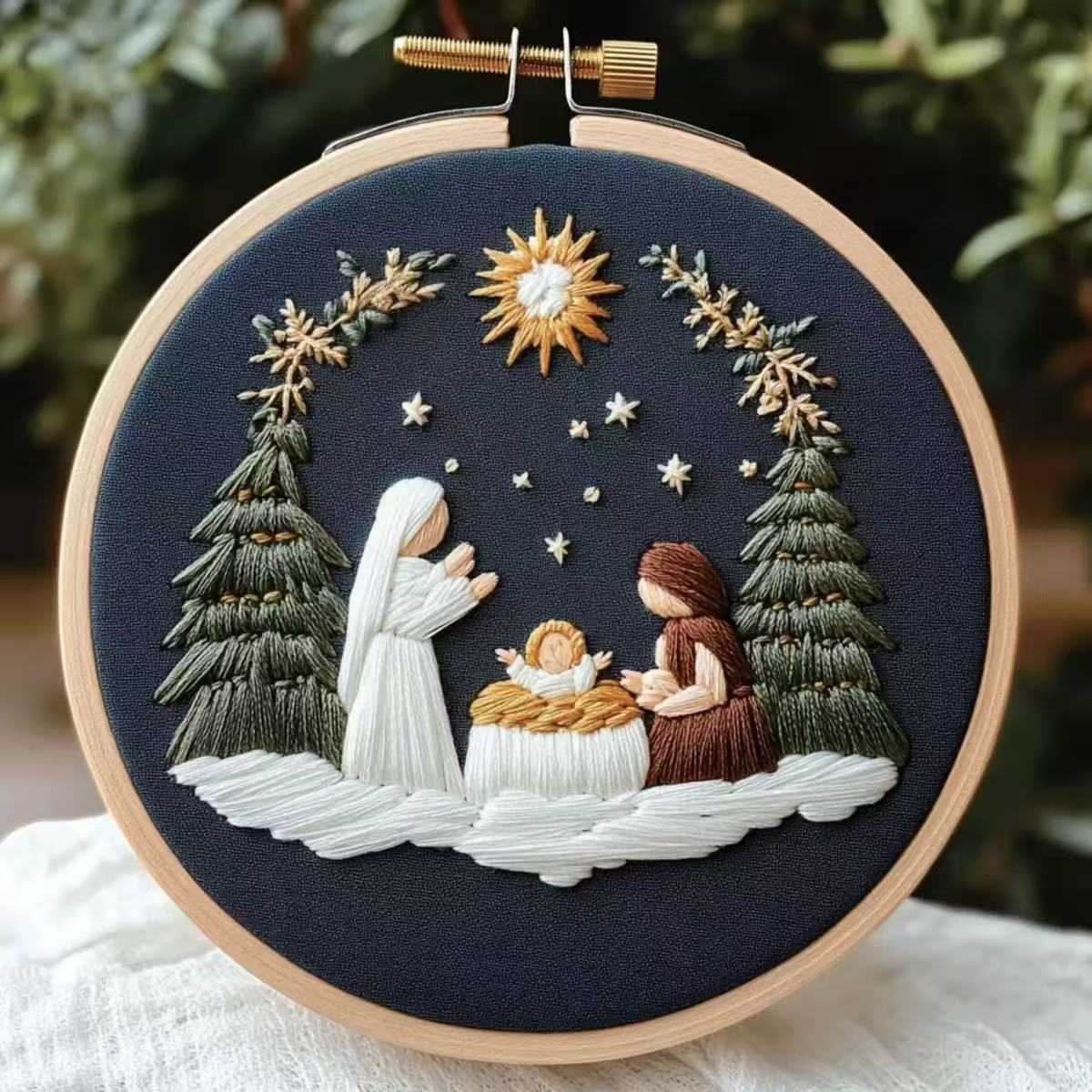 Embroidery of a nativity scene with three figures and trees in a hoop.