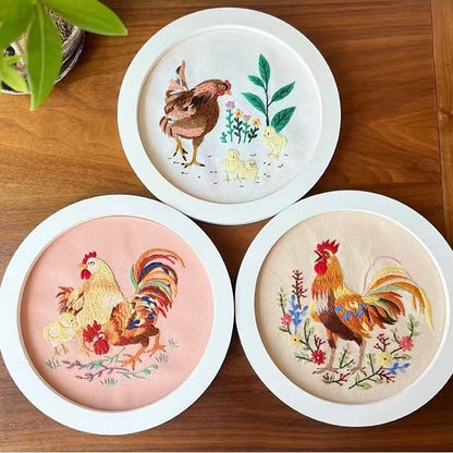 Three embroidered roosters on round white frames on a wooden surface.