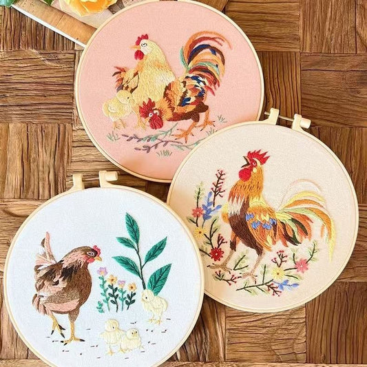 Three embroidered hoops with rooster designs on a wooden surface
