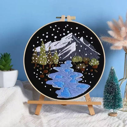 Embroidery hoop with snowy mountain and landscape design on a stand against a blue wall