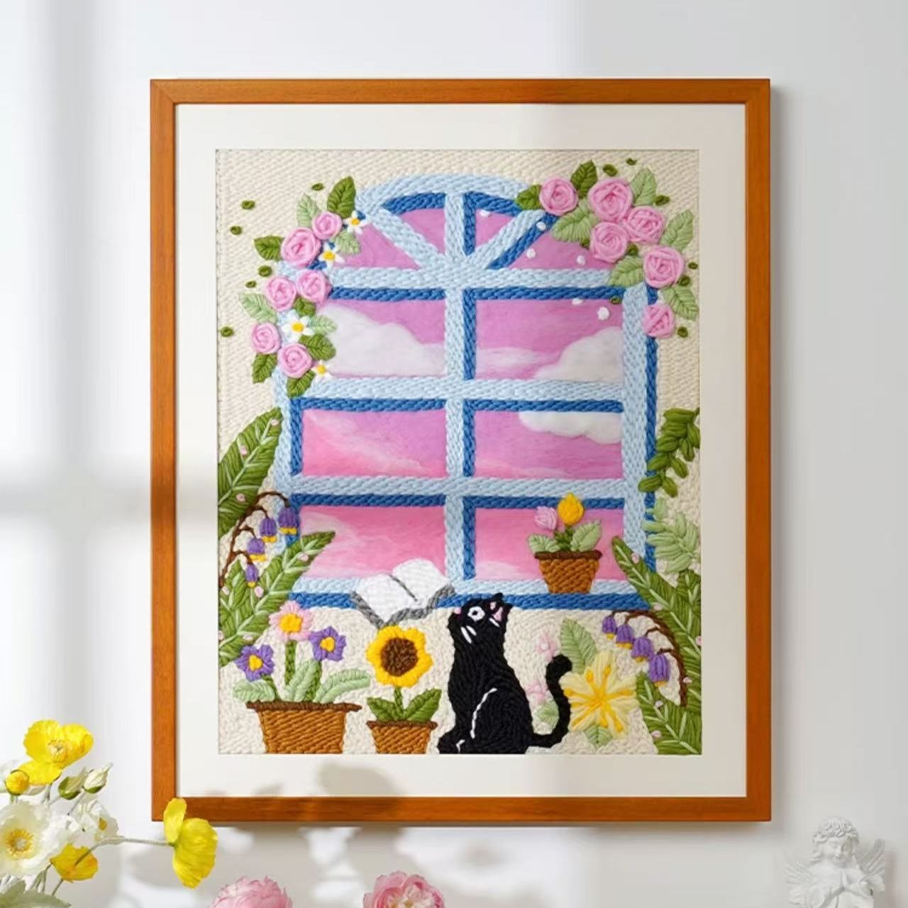 Framed punch needle yarn embroidery art of a window with flowers and a black cat.