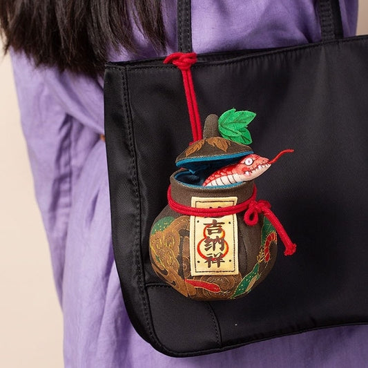 A person carrying a black embroidered gourd bag with a decorative element that resembles a snake